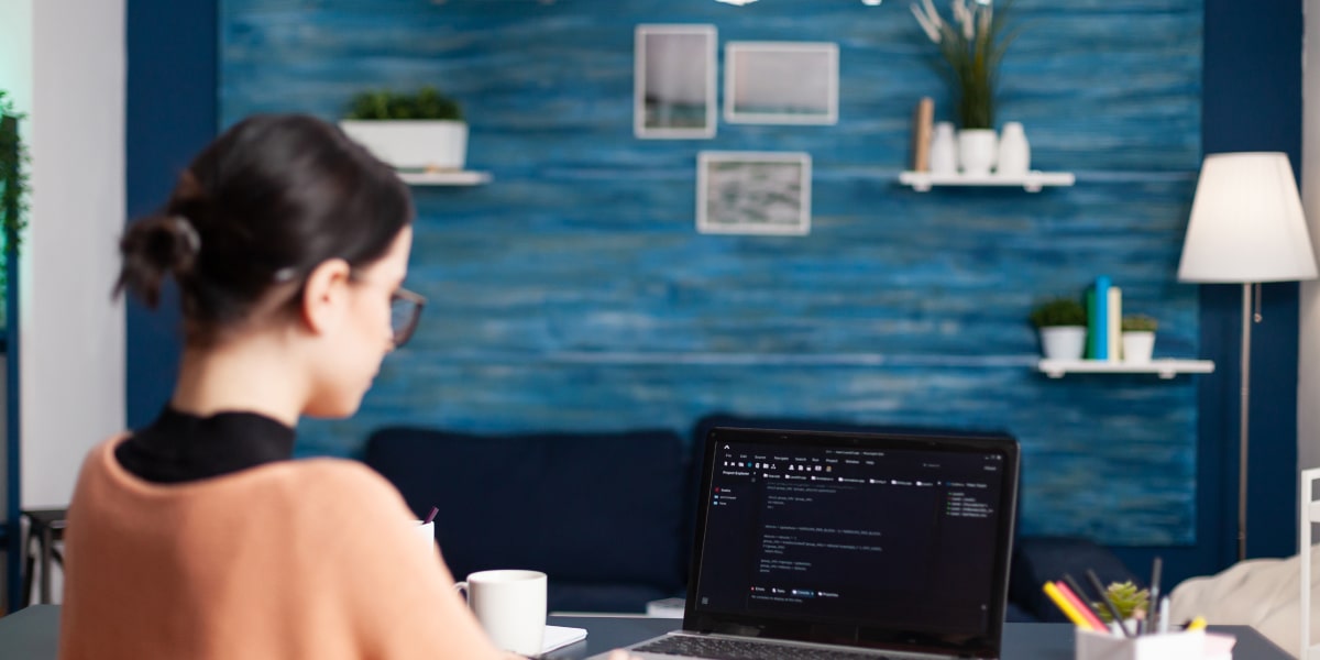 Female JavaScript developer sits at a desk in a startup office, coding on a laptop.