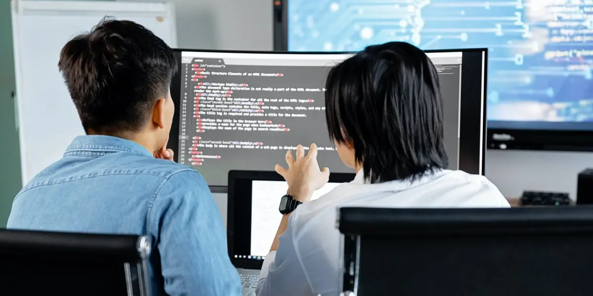 Two designers sitting at a desk with their backs to the camera, looking at some code on a computer