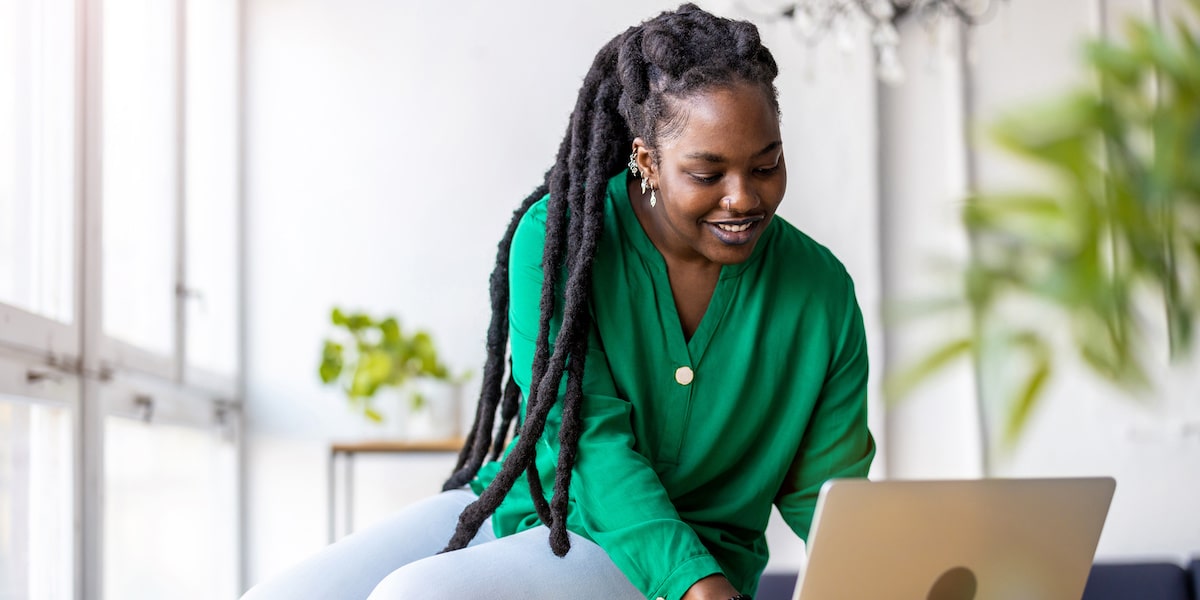 A woman with dreads works at a laptop using her data analyst skills.