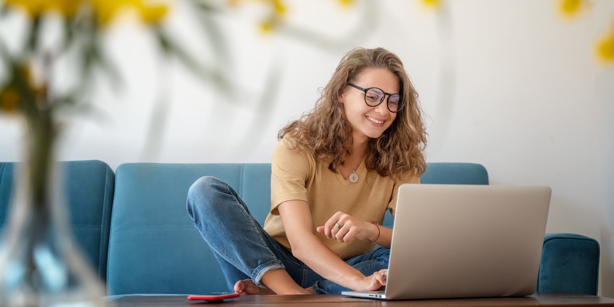 A remote UX designer sitting barefoot on a couch, working on a laptop