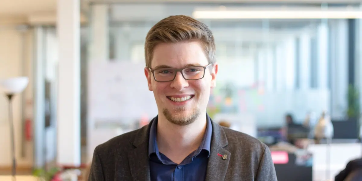 A web developer smiling at the camera in the office of a tech startup.