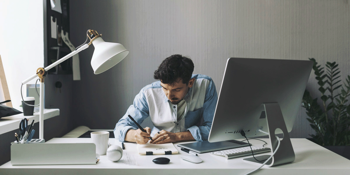 An aspiring UI designer sitting at a desk, writing in a notebook