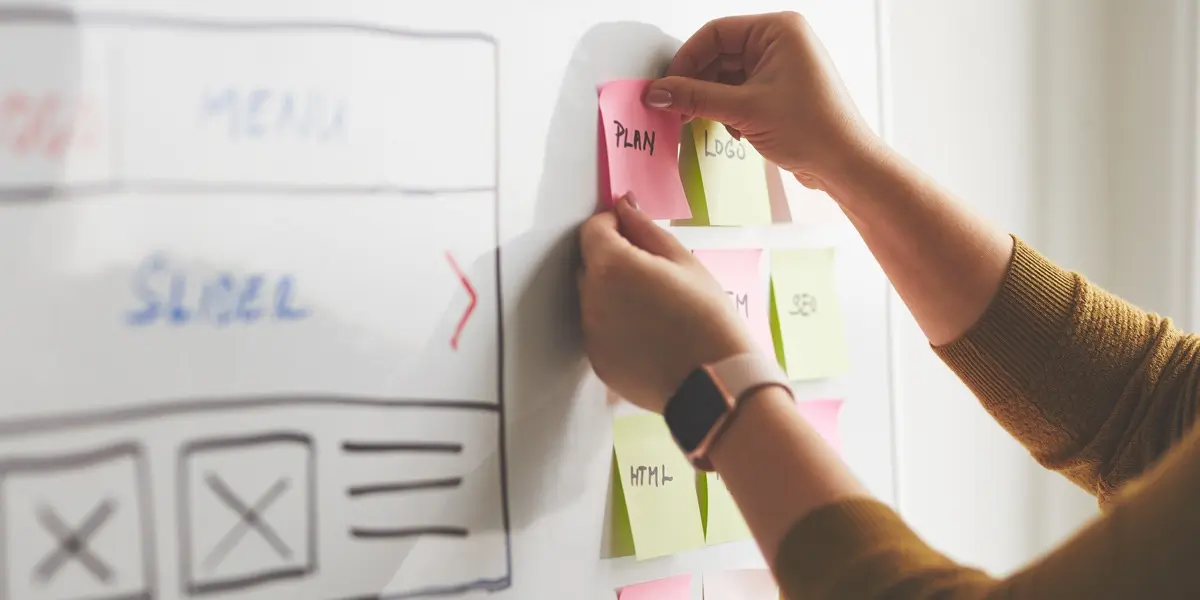Close-up of a UX strategist's hands putting a sticky note on a whiteboard outline of a project