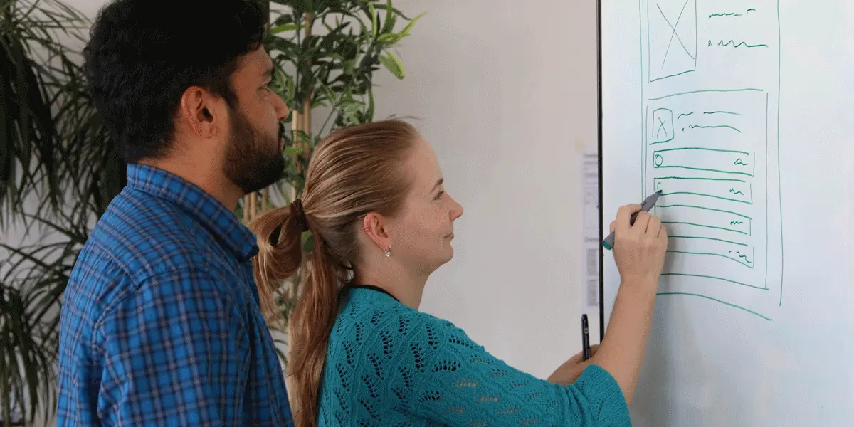 A UX researcher and web developer looking at a whiteboard mockup