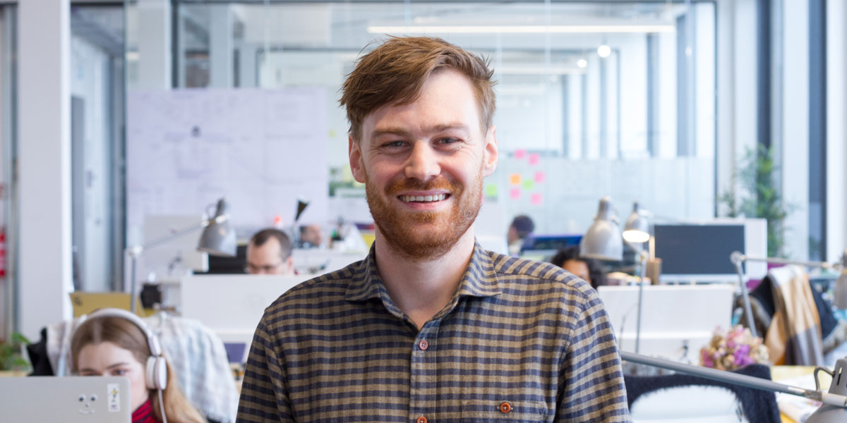A qualified web developer smiles at the camera in a startup office.