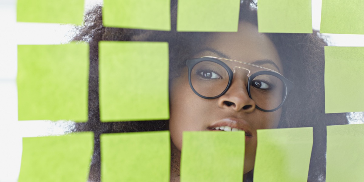 A UX designer peeking through a glas wall covered in sticky notes