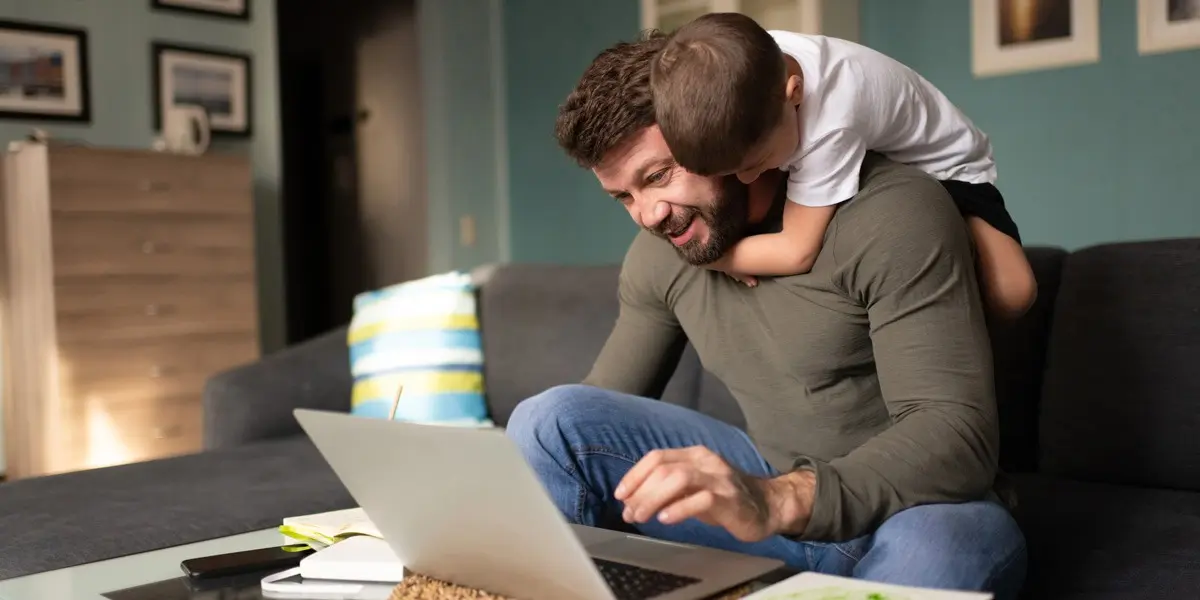 A UX deisgner working from home with his child climbing on his back