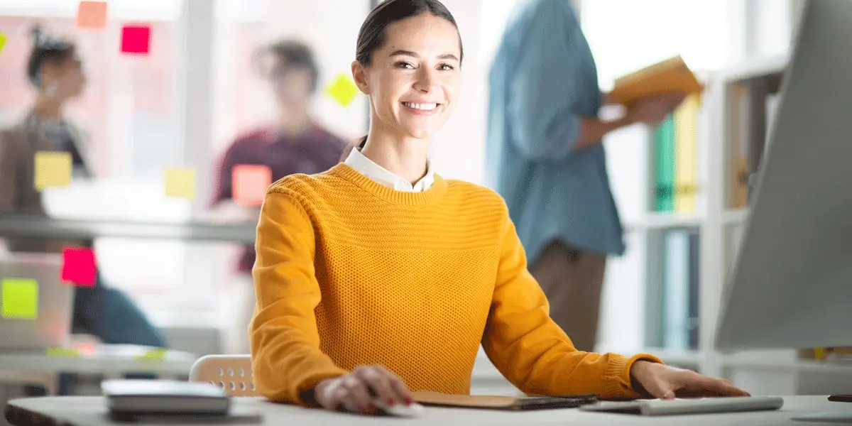 A data analyst sitting at a desk, smiling at the camera