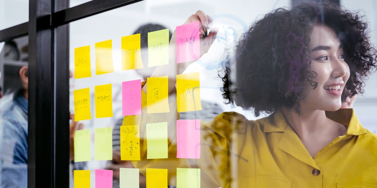 Designer standing behind a glass wall covered in sticky notes describing the difference between UI/UX design