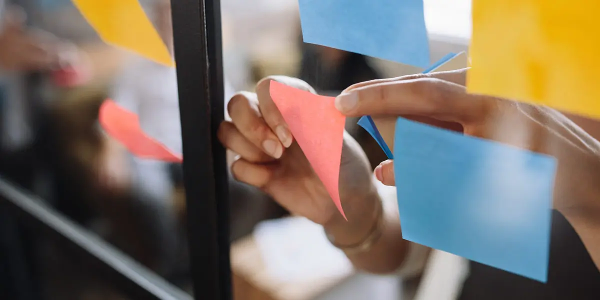 Close-up on a designer's hands, putting sticky notes on a glass wall