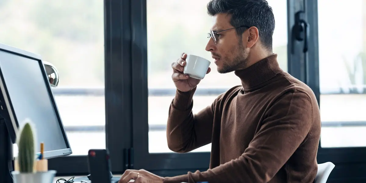 A data analyst in side profile, sipping a cup of tea, looking at a computer screen