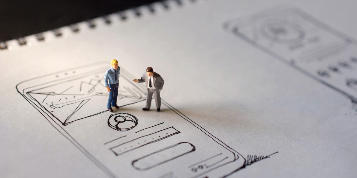 Two plastic toy-sized people standing on a paper prototype sketched in a notebook