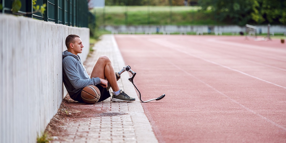 An amputee athlete wearing a runners' prosthetic, sitting next to a track
