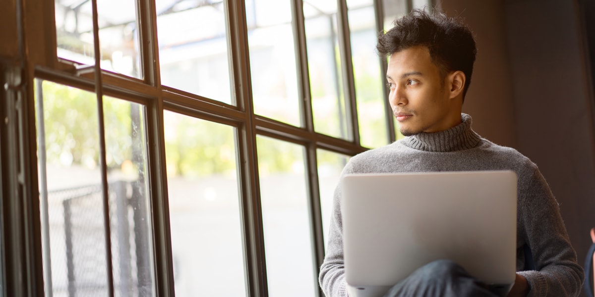An aspiring designer sitting in a windowsill with their laptop