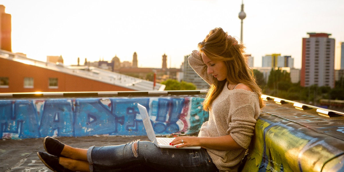 A UX designer sitting on a rooftop patio in Berlin, working on a laptop
