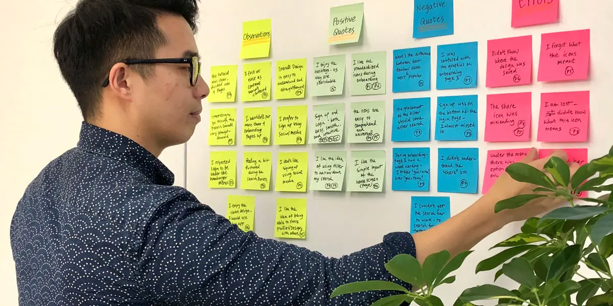 UX designer Ryan Wu standing at a wall covered in sticky notes with research notes