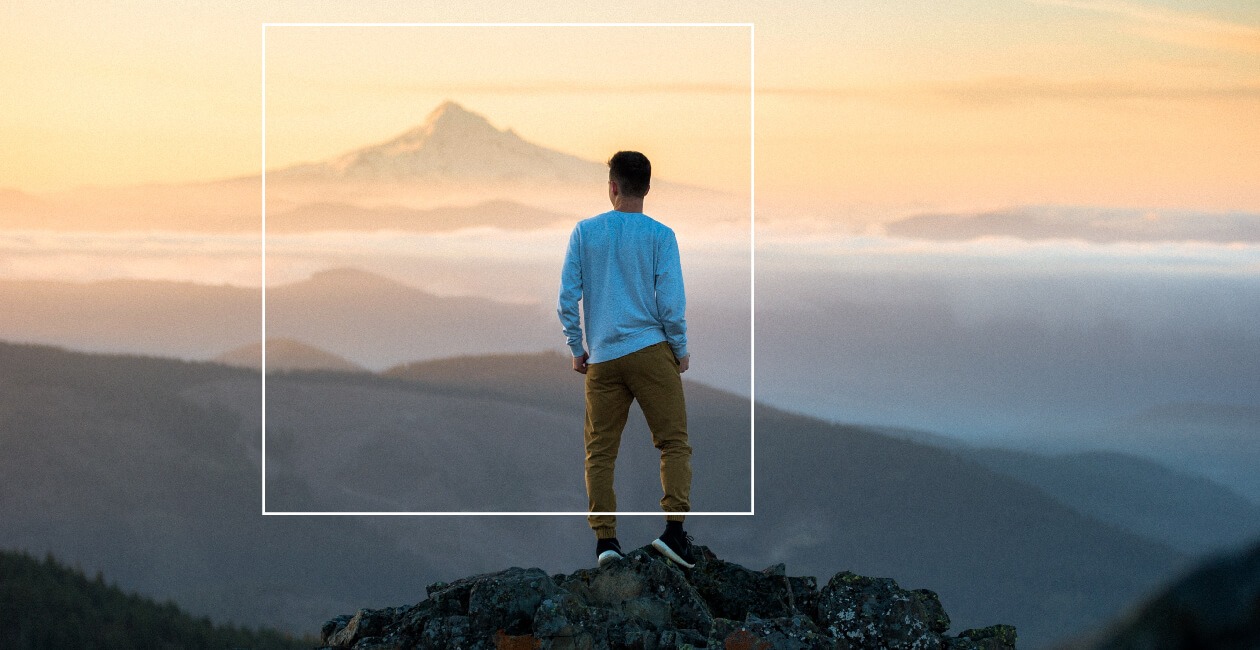 A man stands on a mountain top looking at the horizon.