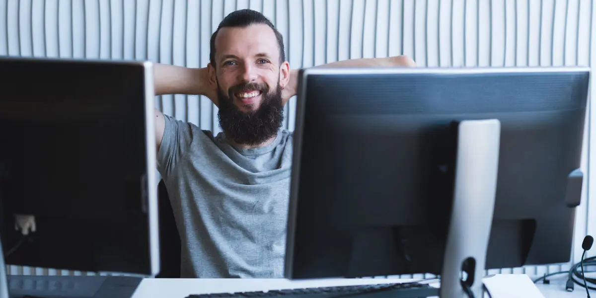 A UX designer smiling behind two computers at a desk learning how to create a user flow