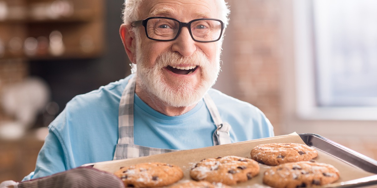 An older man with a beard, baking cookings and smiling
