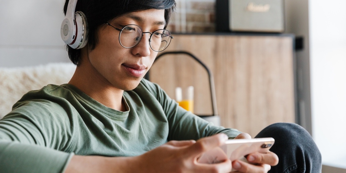 An aspiring designer sitting on a couch, wearing earphones and working on a mobile phone