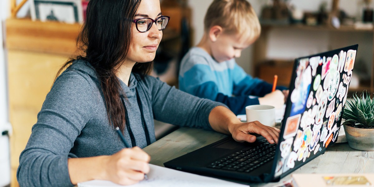 A woman studying a web developer certification program on her laptop with a child beside her.