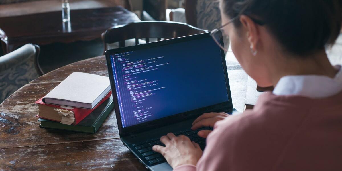 A woman sits coding at a laptop, becoming a web developer.