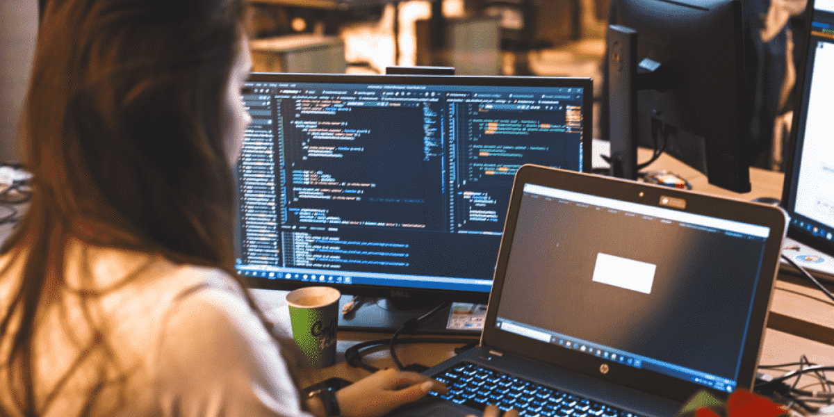 Woman coding on a laptop attached to a monitor.