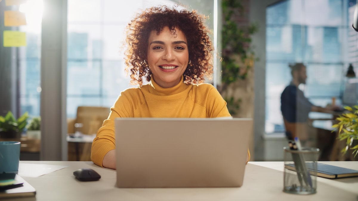 Woman at a laptop learning how to become a web developer smiles at the camera.
