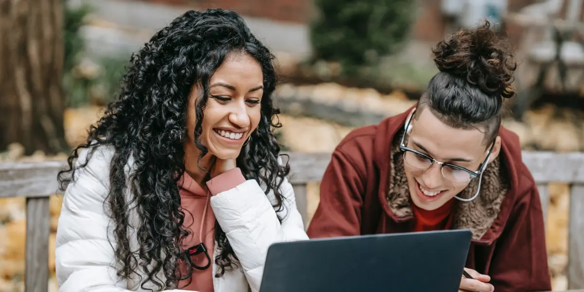 Two designers sitting at a table in a park, looking at a project on a laptop