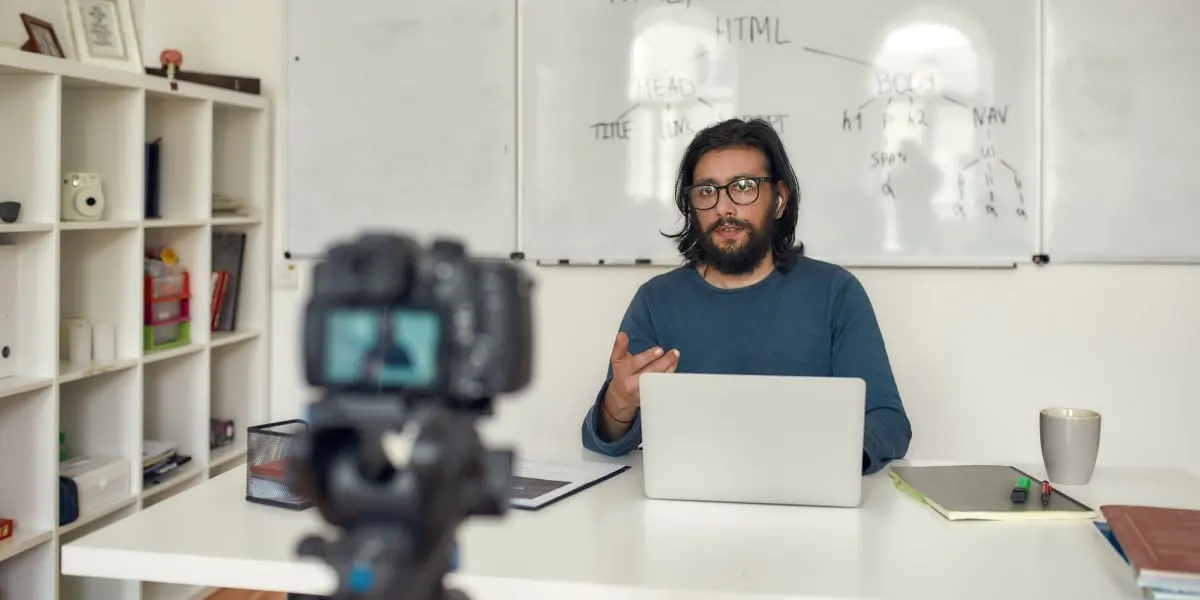 An online coding bootcamp instructor records a video explaining HTML using a camera and laptop.