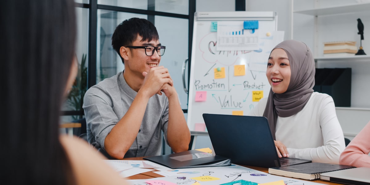 A web developer in a headscarf sits in a brainstorming meeting with her laptop and some other colleagues