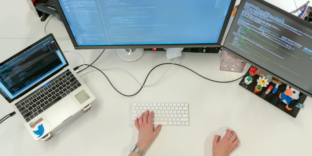 网络开发者坐在两台计算机屏幕和一台笔记本电脑上,与Flask微框架合作