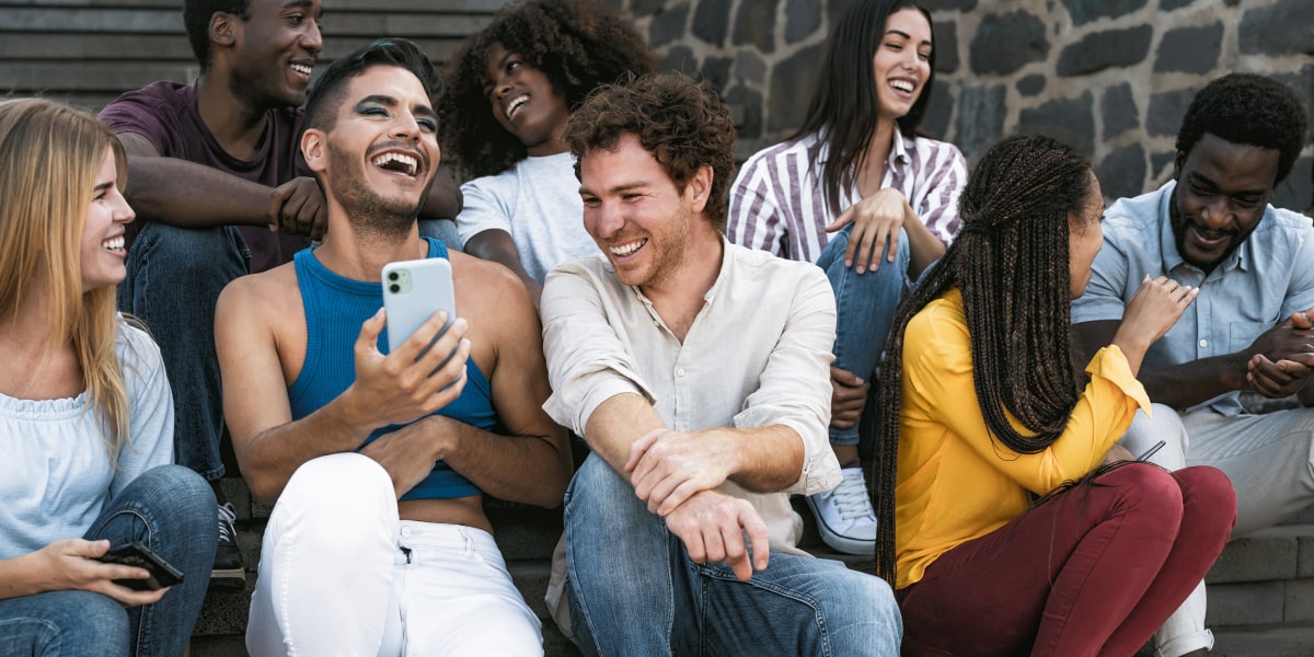 Young group of friends sitting on steps using a smartphone and laughing.