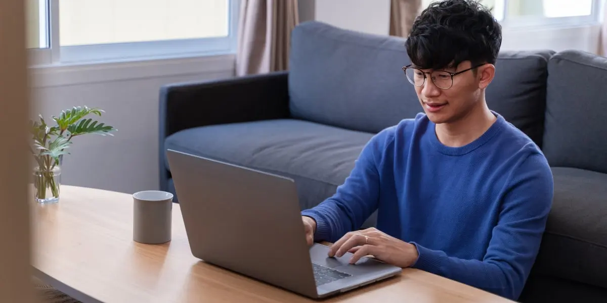 A person sitting on the floor, leaning against a sofa, writing their marketing resume on a laptop