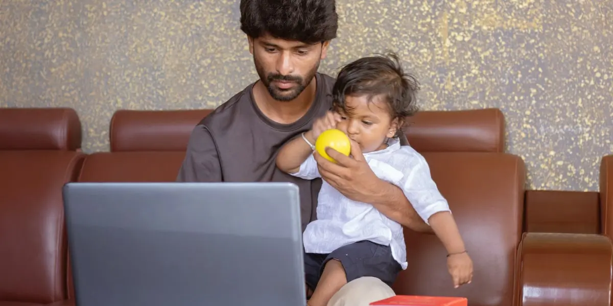 A digital marketing bootcamp student working on a laptop, holding a young child