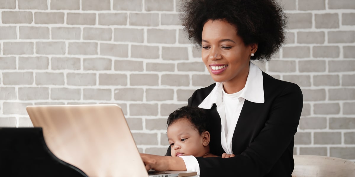 A person sitting with a baby on their lap, working on a computer, planning a performance marketing campaign