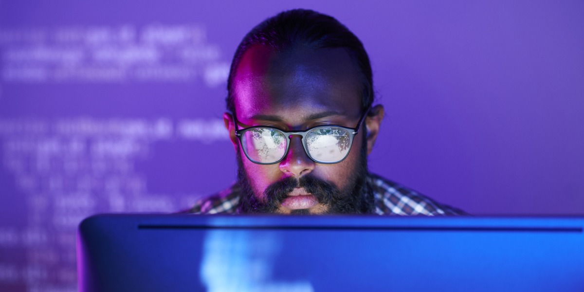 A web developer wearing glasses sits at a computer screen during a hackathon.