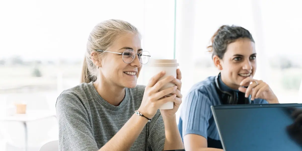 Two aspiring digital marketing analysts sitting at a desk, one holding a cup of coffee and smiling