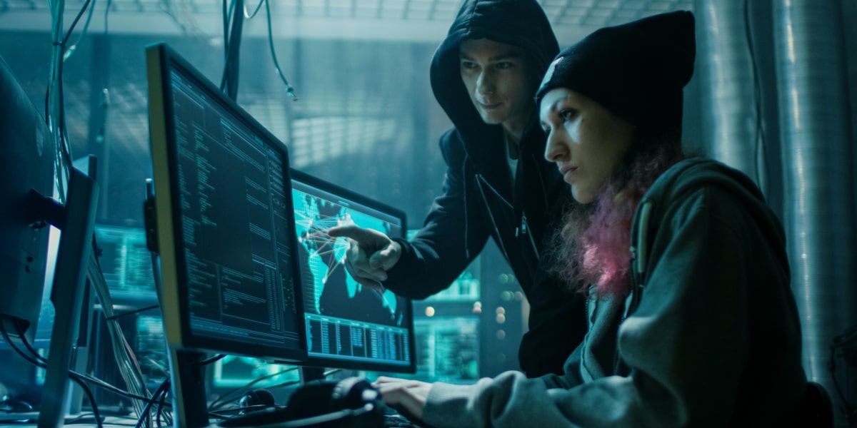 A pair of hackers sit at a computer pointing at the screens