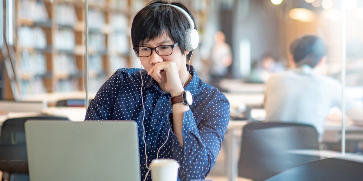 An aspiring marketer sitting at a desk, wearing headphones, researching the best digital marketing certification programs on a laptop