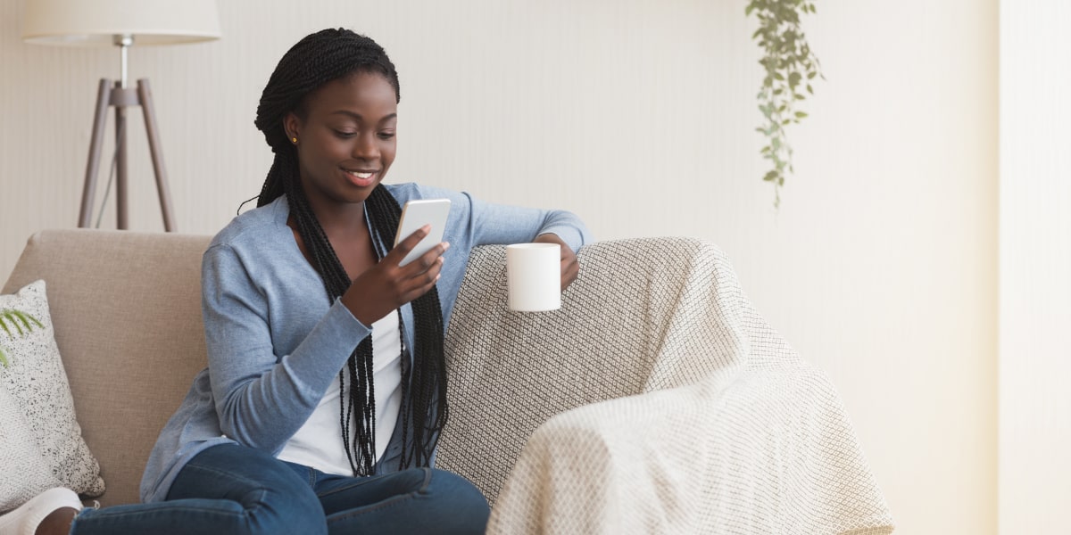 A social media manager sitting on a sofa, holding a mug of tea and looking at a smartphone