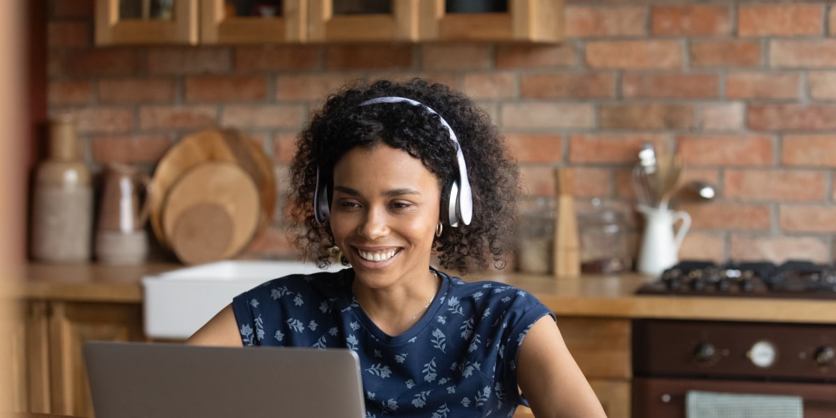 A digital marketing student wearing headphones, smiling, working on a laptop