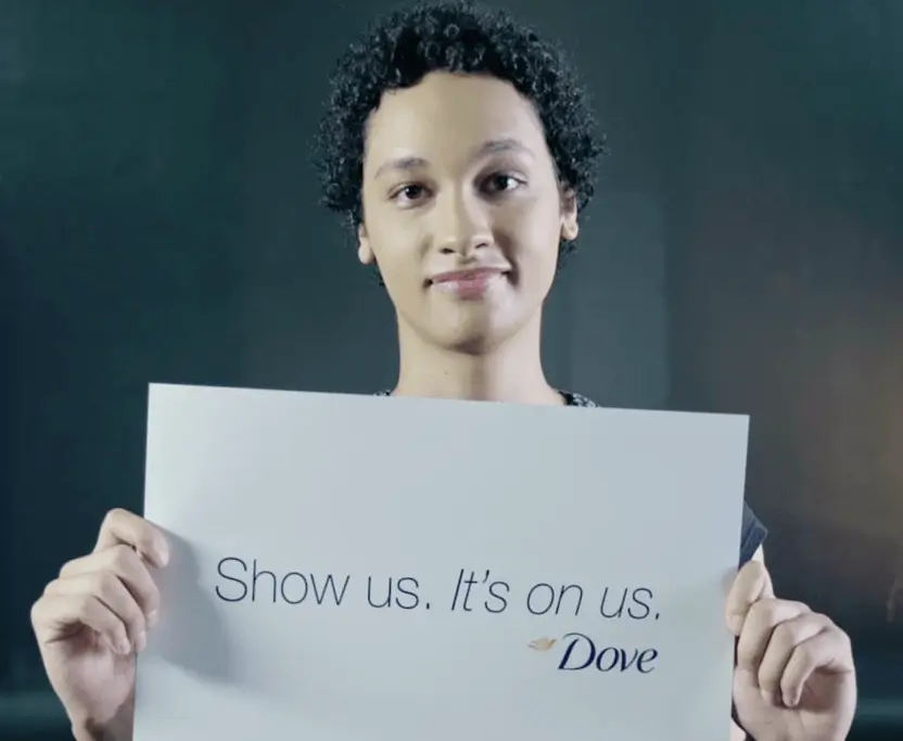 A person holding up a sign saying "Show us. It's on us." as part of a marketing campaign for Dove