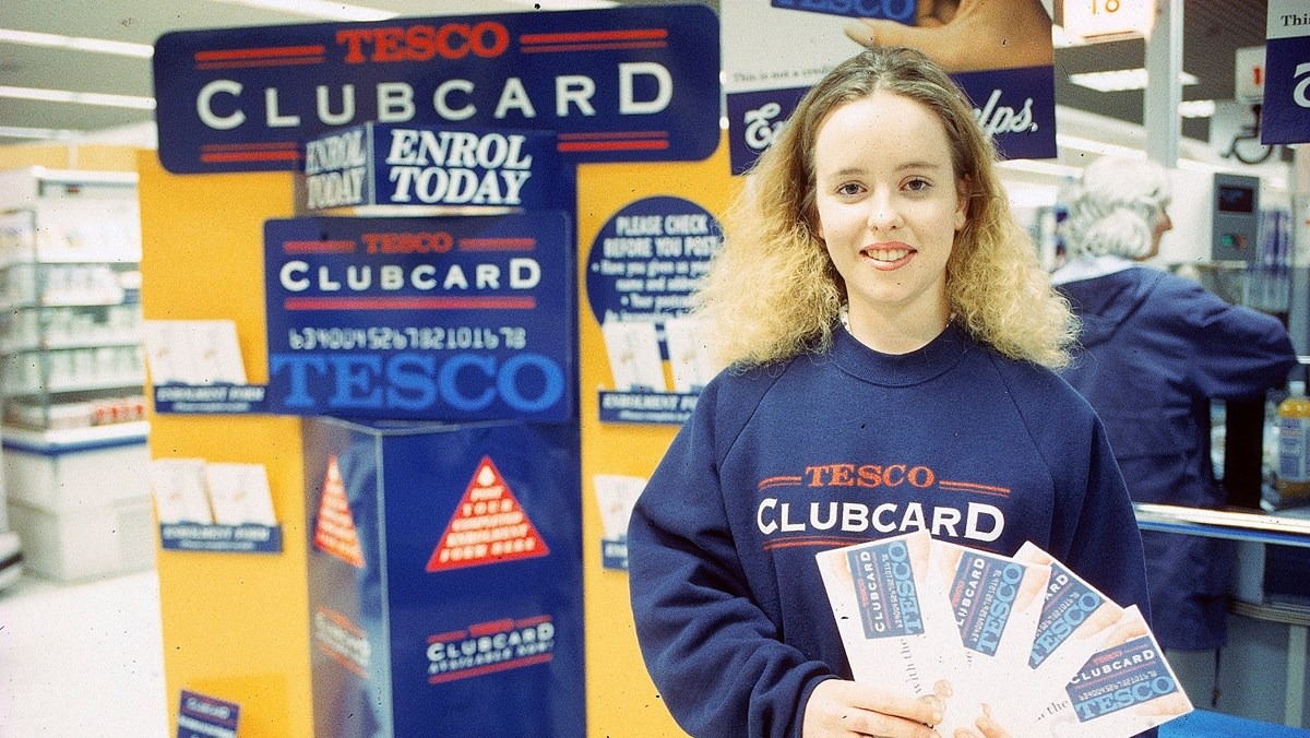 Vintage photograph of a Tesco employee holding Clubcards in front of a Clubcard promotional display