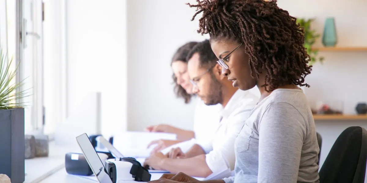 Three designers sitting at a shared desk, working on laptops