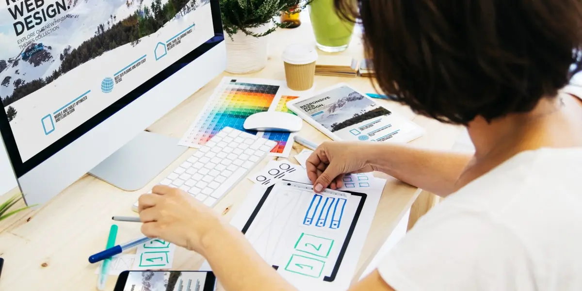 A UI designer sits at her desk working with paper wireframes and color swatches.