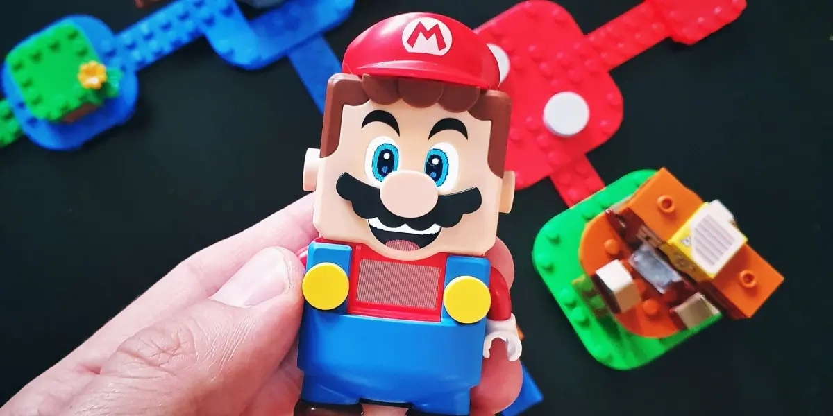 Image of a hand holding a LEGO Super Mario toy with the rest of the toy set in the background.