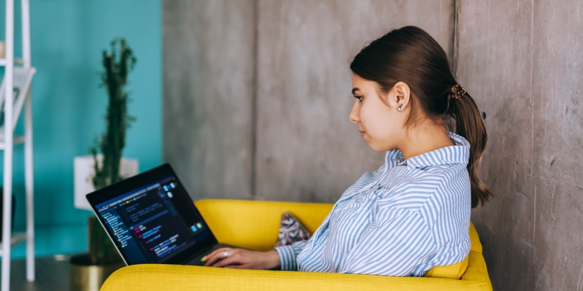 Female coder sitting in a startup office coding on a laptop