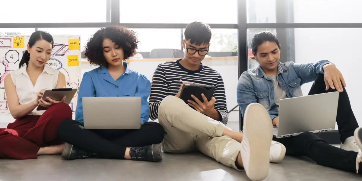 Four students sitting on the floor working on laptops and tablets displaying human-computer interaction.