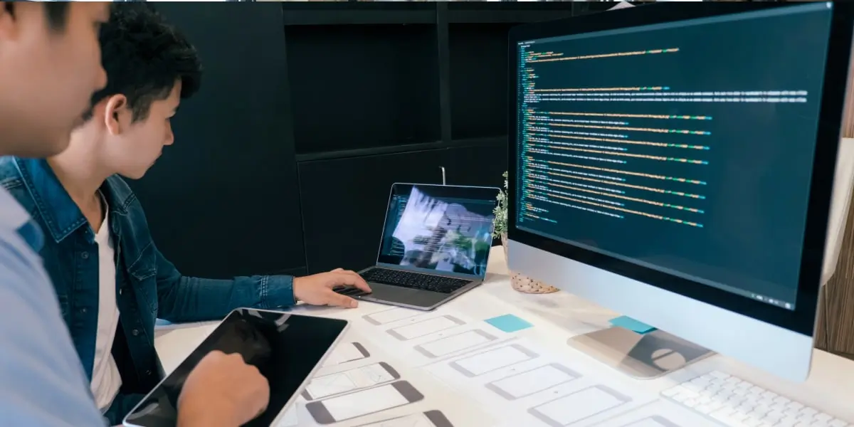 Two UI developers working with paper wireframes and code on a computer screen.